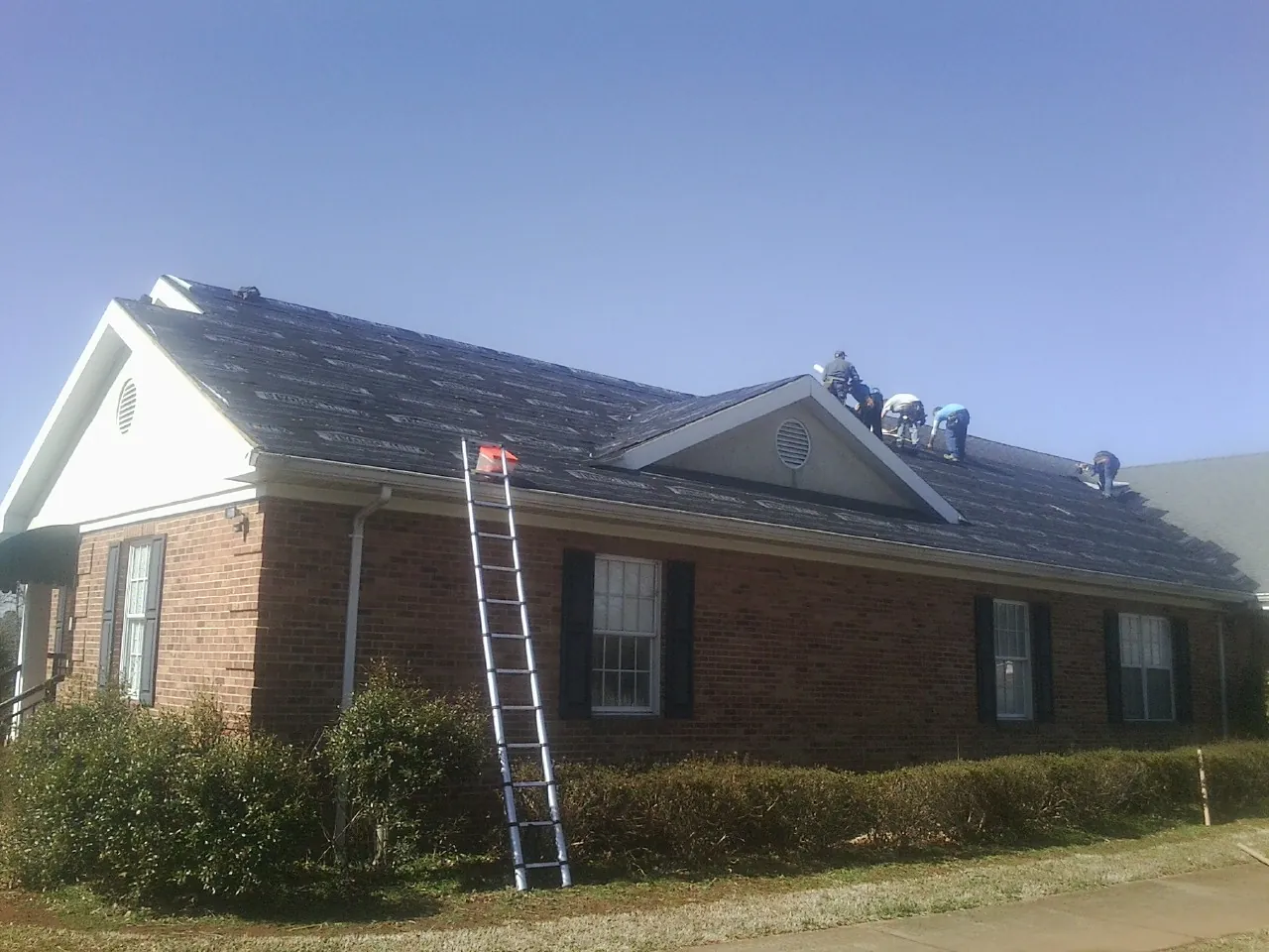 Crew tearing shingles off a brick ranch roof with a ladder set — Metal Roof Repair work by our crew in East Waterboro