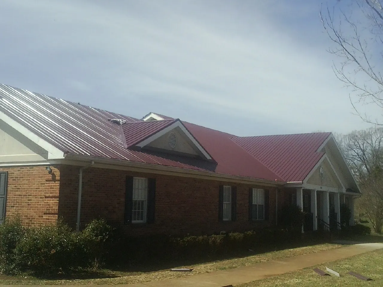 Red metal roof with gabled entries on a long brick building, from a Hail Damage Roof Repair job in East Waterboro