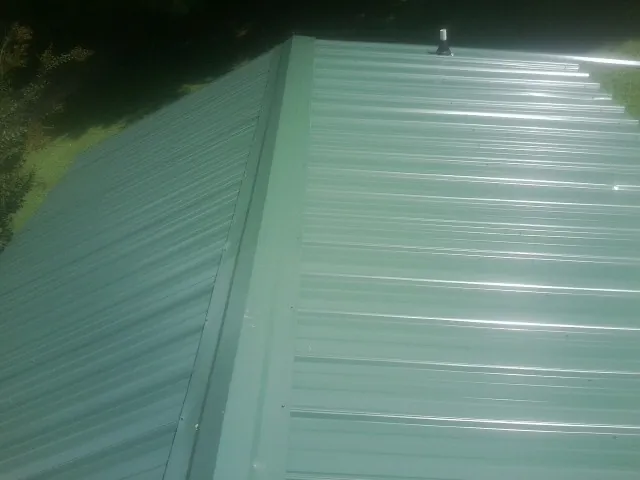 New green metal panels meeting at the ridge of a roof — Flat Roof Repair work by our crew in East Waterboro