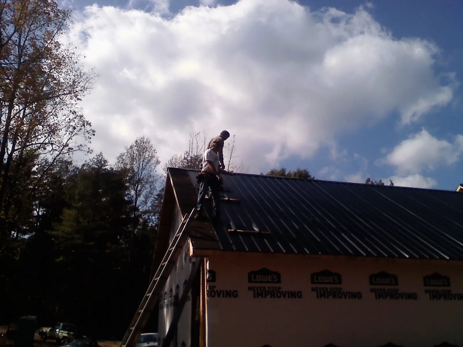 Roofer fastening dark metal panels high against a cloudy sky, from a Roof Inspection job in East Waterboro