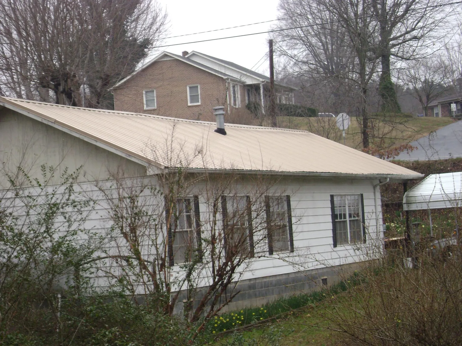 Tan metal roof on a white sided house set into a hillside — Commercial Roofing by Roofing Brothers in East Waterboro